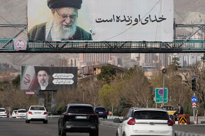 Umferðin gekk sinn vanagang í Teheran í gær og við veginn má sjá skilti með myndum af fyrrum og núverandi æðstuklerkum Írans, Ayatollah Ali Khamenei, sem ráðinn var af dögum í áásum Bandaríkjamanna er í forgrunni og sonur hans, Ayatollah Mojtaba Khamenei, í bakgrunni.