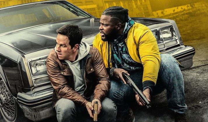 Mark Wahlberg og Winston Duke skýla sér bakvið bíl svo vondu kallarnir geti ekki skotið þá.