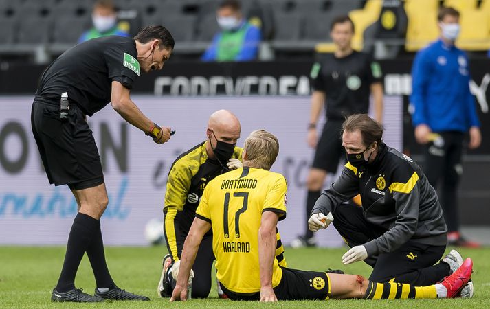 Håland fær hér aðhlynningu frá sjúkraþjálfurum Dortmund sem taka enga áhættu og eru með grímur.