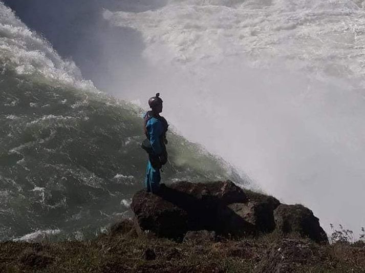 Ferðamaður stillir sér upp við fossbrúnina.