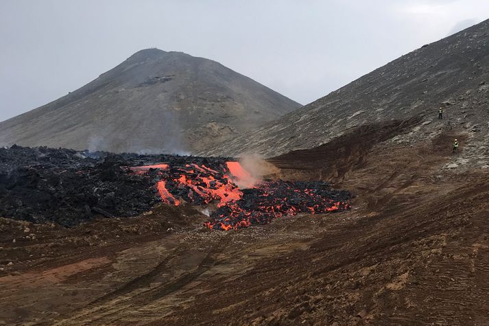 Hraunáin rennur yfir neyðarruðninginn í gær. Starfsmenn fylgjast með uppi í hlíðinni til hægri.