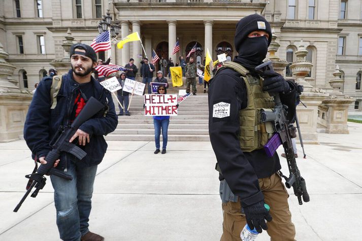 Vopnaðir mótmælendur við ríkisþinghúsið í Lansing í Michigan. Í bakgrunni stendur mótmælandi með skilti þar sem ríkisstjóranum Gretchen Whitmer er líkt við nasistaforingjanna Adolf Hitler vegna sóttvarnaaðgerðanna.