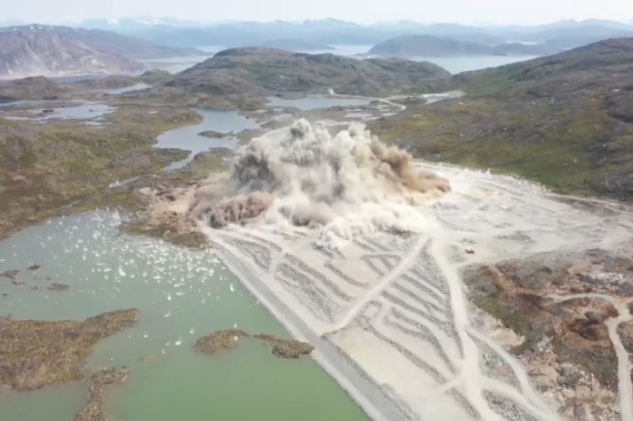 Stærsta sprenging í sögu Grænlands. Verktakinn notaði 230 tonn af sprengiefni til að sprengja 321 þúsund rúmmetra af klöpp. Sjá má hvernig grjótinu rignir út á flóann vinstra megin og upp í hlíðarnar hægra megin.