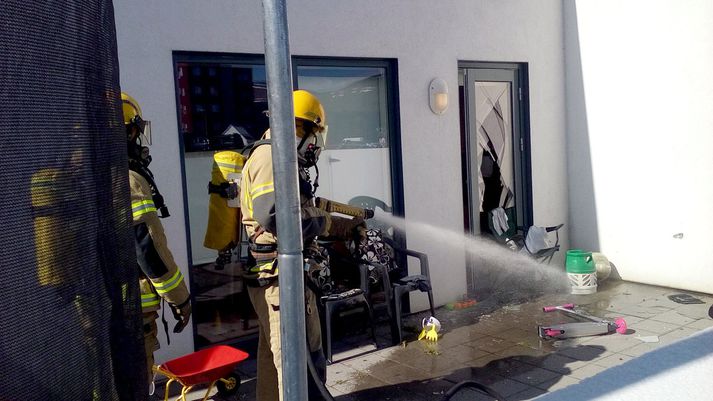 Slökkviliðsmenn að störfum, á myndinni kæla þeir niður annan gaskút á pallinum. Hér sést vel hversu öflug sprengingin var, glerhurðin í molum.