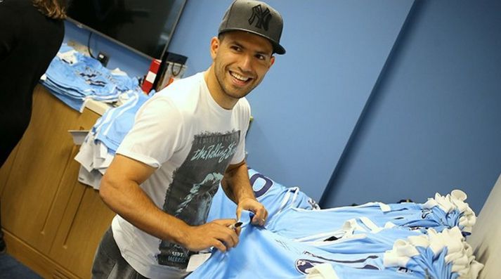 Aguero með pennann á lofti og margar treyjur bíða hans þarna.