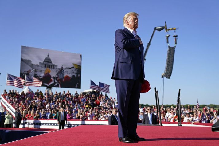 Trump hlýðir á kór uppreisnarmanna við upphaf fjöldafundar í Waco í Texas í gær. Fyrir aftan hann voru sýndar myndir frá árásinni á þinghúsið 6. janúar 2021.