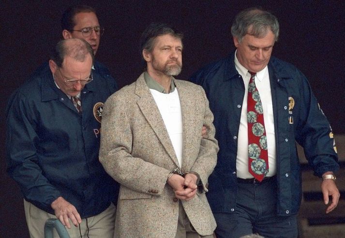 Ted Kaczynski (í handjárnum) árið 1996. Hann var stærðfræðingur að mennt og kenndi við háskóla áður en hann snerist til öfgahyggju og hóf áralanga hryðjuverkaherferð. Hann var greindu með ofsóknargeðklofa en bannaði lögmönnum sínum að bera það fram sem vörn í málinu.