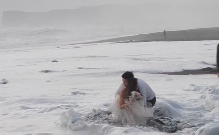 Brúðarkjóllinn var þungur eftir að aldan skall á hann, að sögn leiðsögumanns sem festi atvikið á filmu. Hún segir ferðamenn ganga skugglega langt að sjónum í fjörunni þrátt fyrir nýtt viðvörunarkerfi.