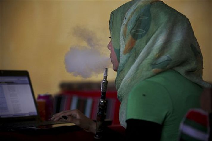 Múslimakona reykir vatnspípu meðan hún vafrar á netinu á Gaza ströndinni.