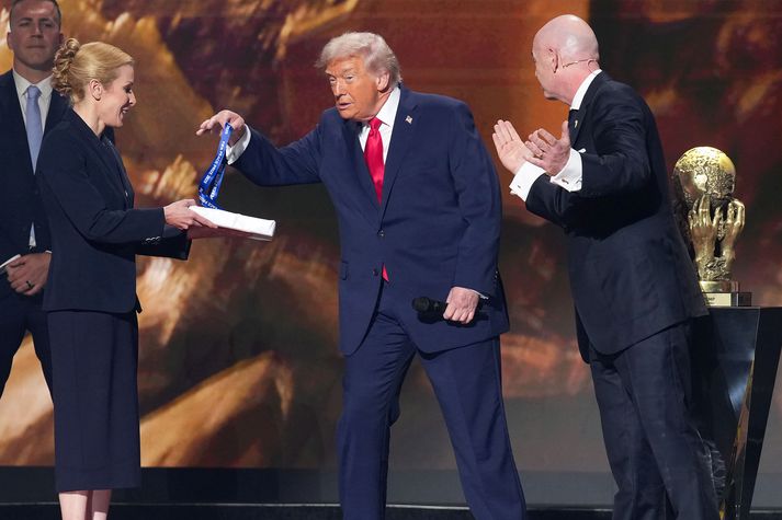 Donald Trump teygir sig í verðlaunapeninginn fyrir að vera fyrsti viðtakandi Friðarverðlauna FIFA.