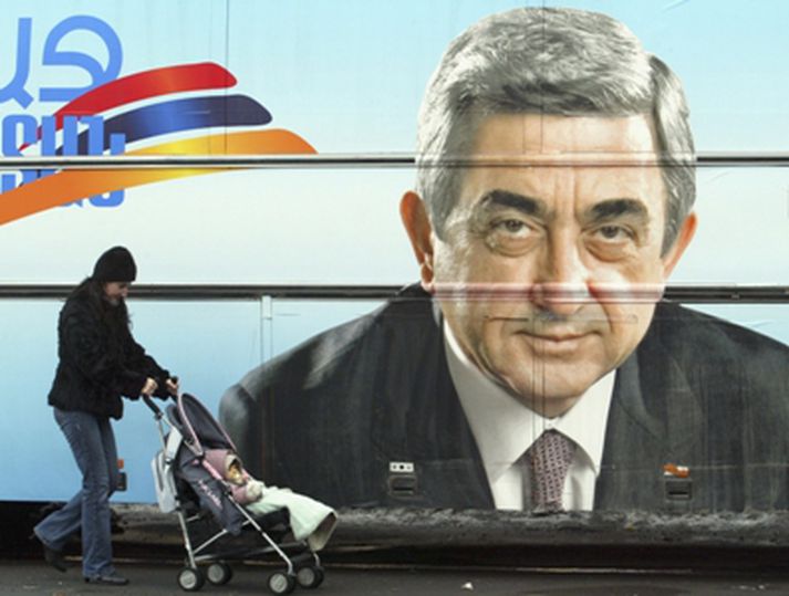 Kona með kerru gengur framhjá auglýsingaspjaldi eins frambjóðandans, Serzh Sarkisian, sem er núverandi forsætisráðherra landsins.