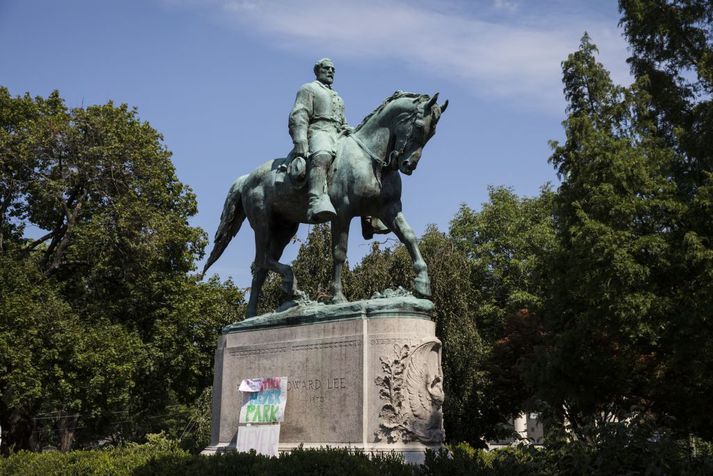 Styttan af Robert E Lee ásamt plaggötum sem krefjast þess að garðurinn Lee Park verði endurnefndur Heyer Park til minningar um konuna sem dó þegar keyrt var inn í þvögu mótmælenda.