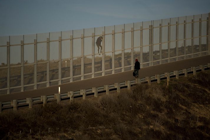 Menn klifra yfir girðingu á landamærum Mexíkó og Bandaríkjanna.