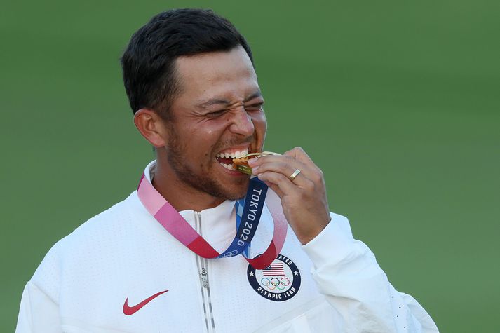 Xander Schauffele bítur í Ólympíugullverðlaunapening sinn sem hann vann í Tókýó 2021.
