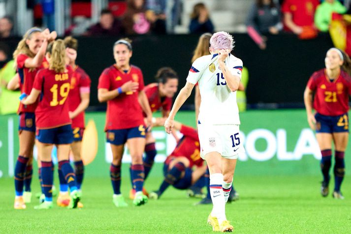 Megan Rapinoe gengur mjög svekkt af vell á meðan þær spænsku fagna góðum sigri.