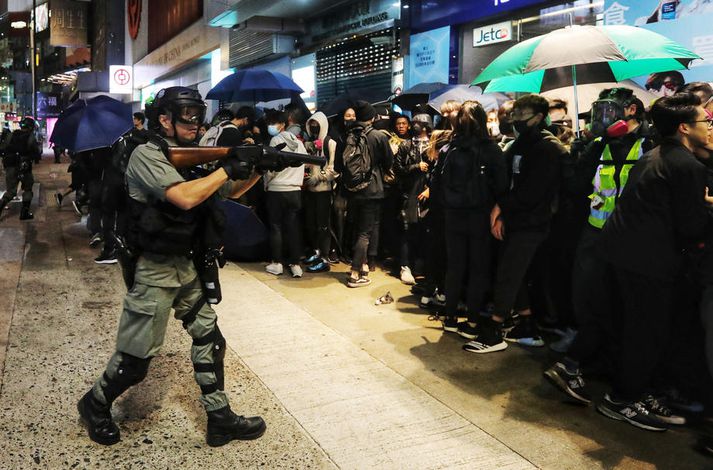 Óeirðarlögreglumaður beinir skotvopni að mótmælendum í Hong Kong á nýársdag.