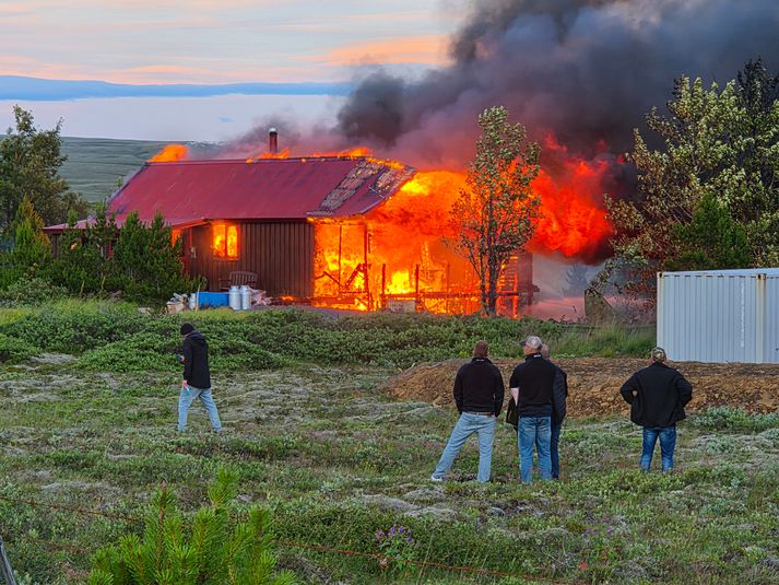 Húsið stendur í ljósum logum. Hvort fólkið í forgrunni dvaldi í sumarhúsinu er ekki vitað.