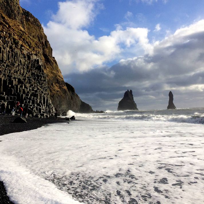 Stuðlabergið í Reynisfjöru er vinstra megin á myndinni. Mikill munur er á flóði og fjöru hve langt sjórinn nær að berginu.