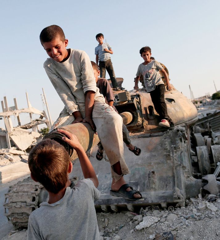 Sýrlensk börn leika sér á ónýtum skriðdreka. Myndin er tekin skammt frá bænum Kobane sumarið 2015.