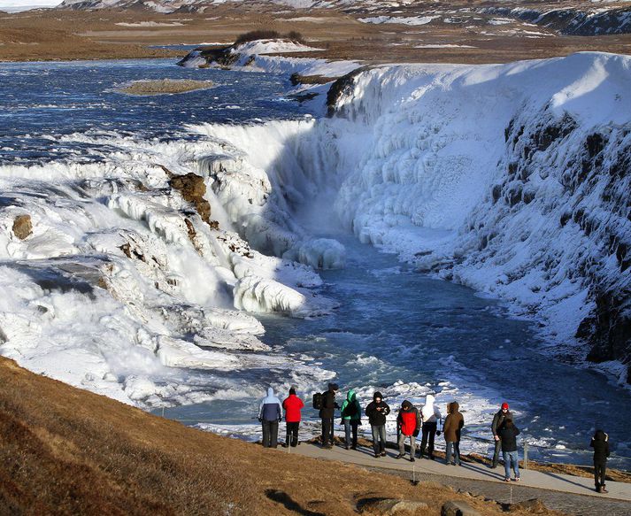 Gullfoss í Klakaböndum með ferðamenn sér við hlið.