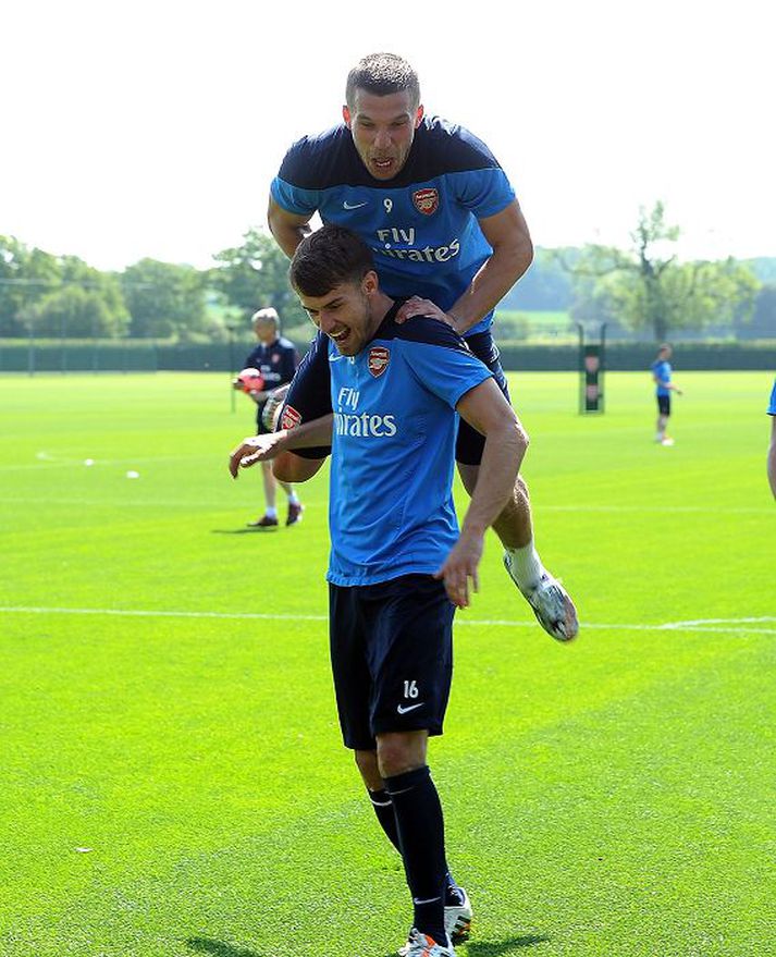 Lukas Podolski stekkur á bak Aarons Ramsey.