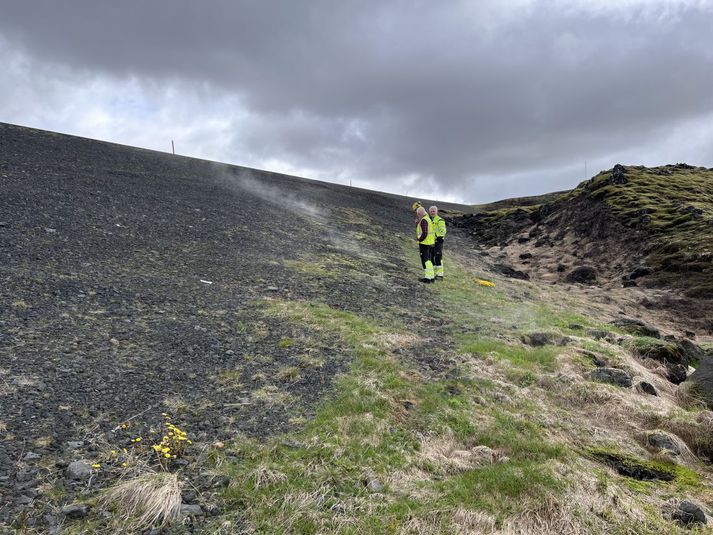 Starfsmenn Vegagerðarinnar virða fyrir sér rjúkandi vegfláa við hringveginn í Hveradalsbrekku.