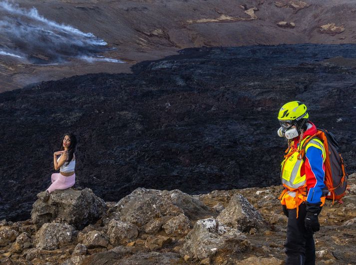 Áhrifavaldur í myndatöku og björgunarsveitarmaður með gasgrímu við gosstöðvarnar um helgina.