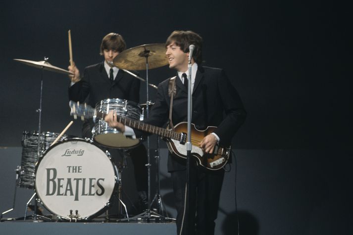 McCartney slær á strengi bassans fræga á meðan félagi hans Ringo Starr lemur skinnin fyrir aftan hann árið 1964.