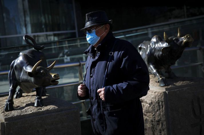 Karlmaður með andlitsgrímu gengur fram hjá styttum fyrir utan banka í Beijing í Kína í morgun. Hröð lækkun á mörkuðum í Asíu stöðvaðist þegar þeir opnuðu í morgun og náðu þeir sér aðeins á strik.