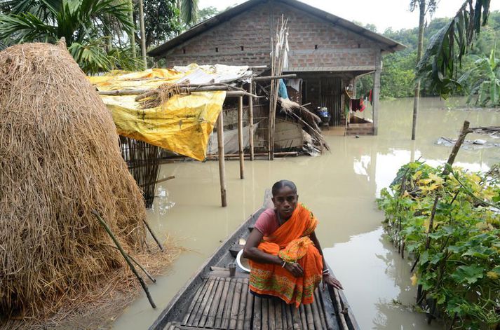 Kona situr á bát við hús sitt sem er á floti vegna flóðanna í Chandrapur í Kamrup-héraði í Assam.