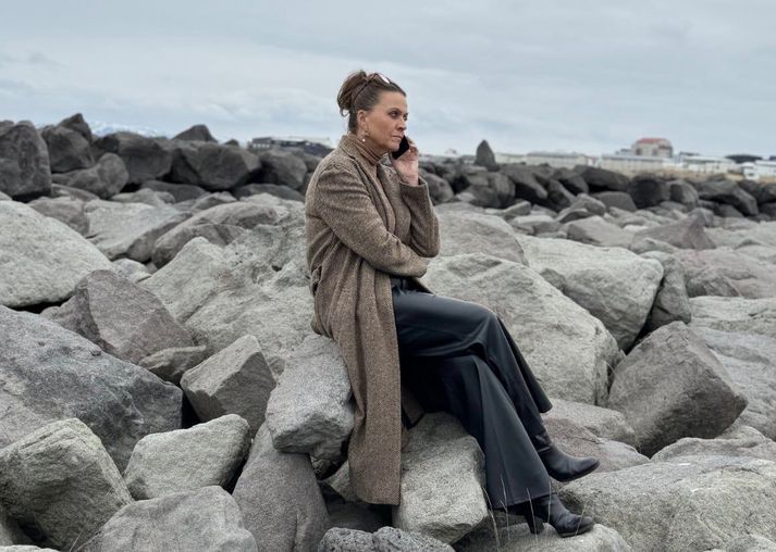 Steinunn Ólína forsetaleg, með símann uppi við, sitjandi á steini á Reykjanesi.