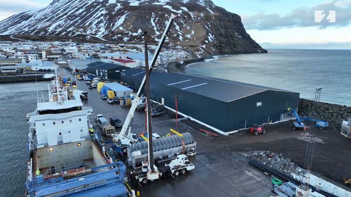 Húsið er risið í Bolungarvíkurhöfn. Við bryggjuna liggur flutningaskip sem er að flytja tækjabúnað fyrir vinnsluna.