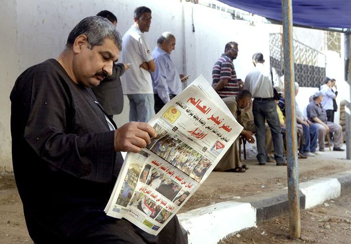 Þessi las blöðin á meðan kjósendur biðu í röð við kjörstað í Kaíró.