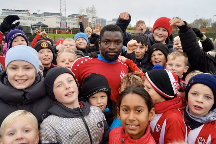 Isaac ásamt fjölda barna sem mættu á fótboltaleik til stuðnings Isaac. Samfélagið í Laugardalnum segir Isaac vera ómetanlegt og hann er spenntur að snúa aftur til starfa hjá Þrótti.