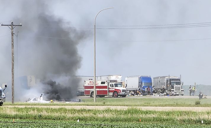 Svartur reykur stígur frá flaki rútunnar á slysstað í Manitoba-fylki. Vitni segist hafa séð viðbragðsaðila reyna að bjarga fólki út úr brennandi rútunni.