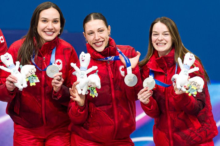 Florence Brunelle er hér í miðjunni og sýnir stolt verðlaunapeninginn með höndinni sem vantar á fingurna. Með henni eru liðsfélagarnir Courtney Sarault og Kim Boutin.