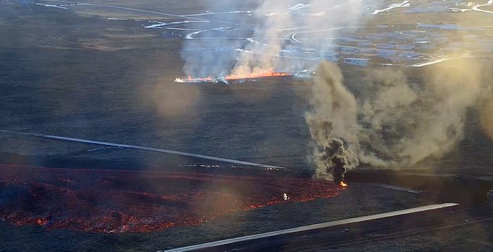 Nýja sprungan séð úr vefmyndavél. Hraunið úr fyrri sprungunni færist hægt meðfram varnarveggnum.