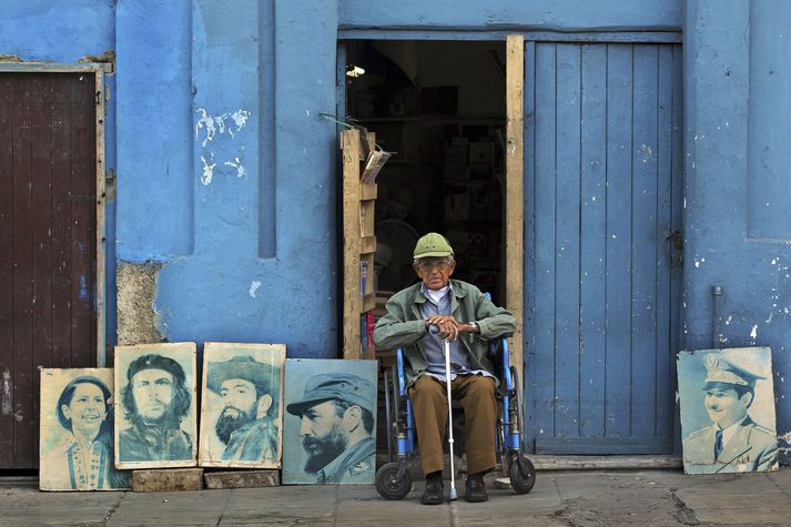 Aldraður maður hefur stillt upp ljósmyndum af Castro og fleiri byltingarhetjum í höfuðborginni Havana þar sem hann situr á gangstéttinni í hjólastól sínum.