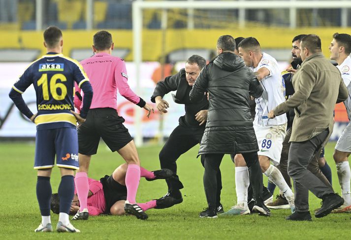 Halil Umut Meler liggur hér í grasinu eftir höggið frá Faruk Koca, forseta MKE Ankaragucu félagins, sem stendur yfir honum.