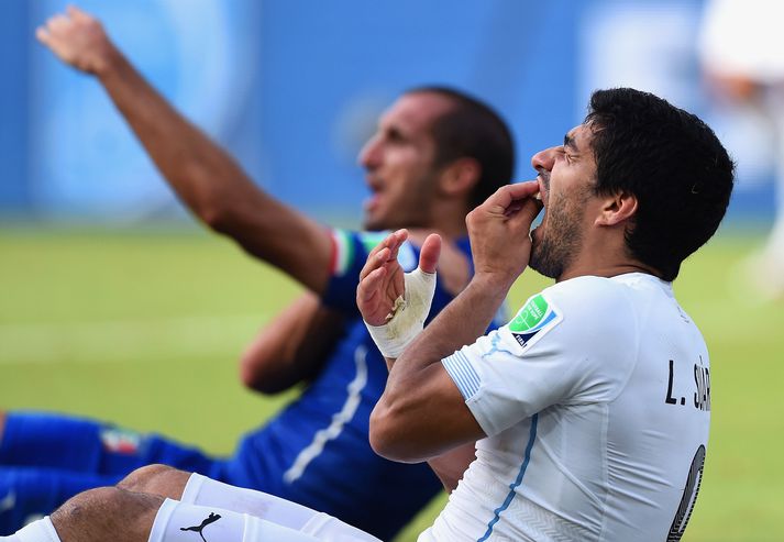 Luis Suarez kvartar undan verk í tönnunum eftir að hafa bitið Ítalann Giorgio Chiellini sem sést í bakgrunni halda um öxlina þar sem mátti sjá far eftir bit Úrúgvæans.