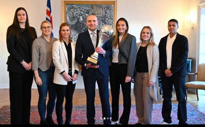 Guðni Th. Jóhannesson, forseti Íslands, heldur hér á Forsetabikarnum við hlið nokkurra leikmanna íslenska landsliðsins. Leikmennirnir eru Hafdís Renötudóttir, Hildigunnur Einarsdóttir, Þórey Rósa Stefánsdóttir, Berglind Þorsteinsdóttir, Perla Ruth Albertsdóttir og Thea Imani Sturludóttir.