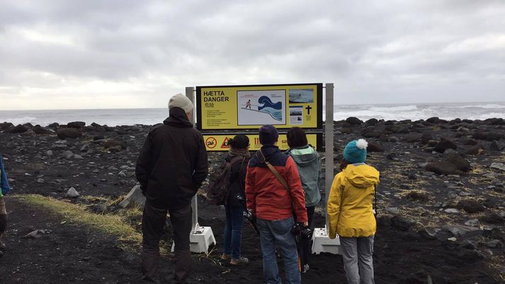 Ferðamenn skoða nýja öryggisskiltið í Reynisfjöru.