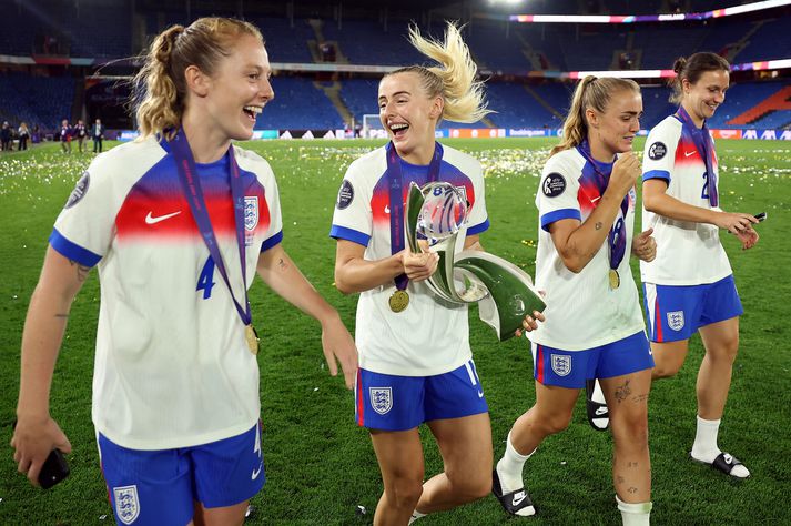 Chloe Kelly fagnar með bikarinn og við hlið liðsfélaga sinna í Evrópumeistaraliði Englands.