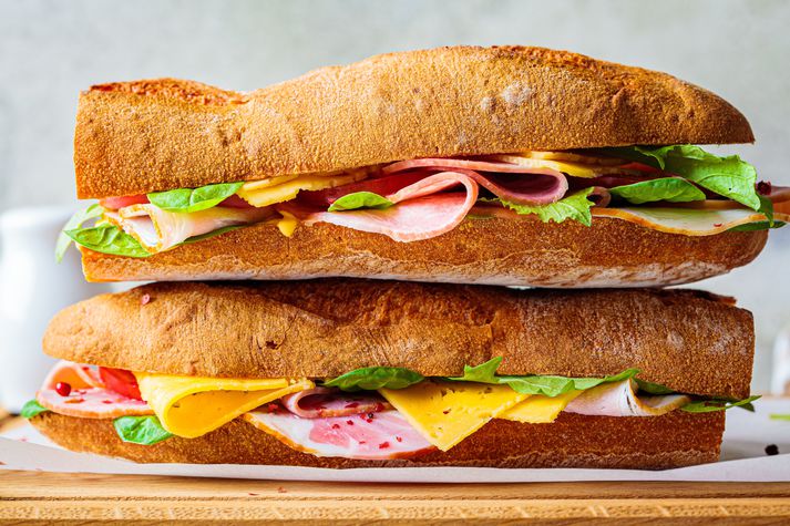 Baguette sandwiches with meat, cheese and vegetables on wooden board.