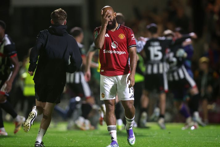 Bryan Mbeumo skúrkur Manchester United heldur um andlitið á sér á meðan leikmenn Grimsby Town fagna sigri.