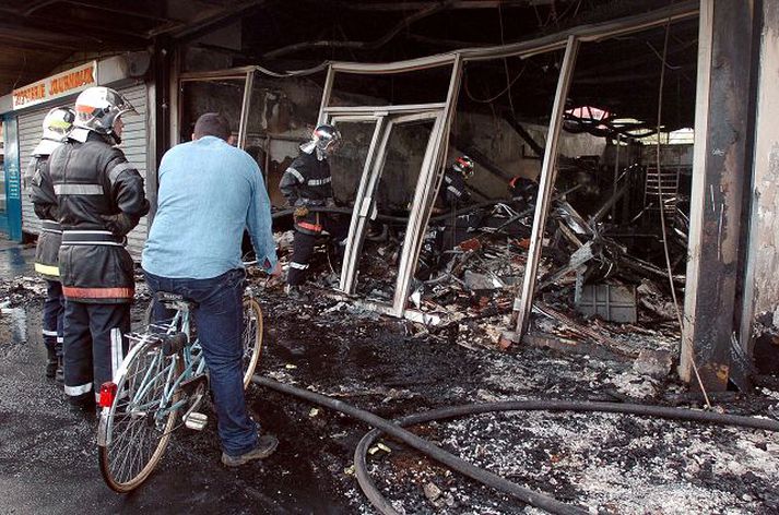 Frá Evreux. Slökkviliðsmenn standa við búð í bænum Evreux í Mið-Frakklandi sem óeirðaseggir rústuðu og kveiktu í. Útgöngubann tók gildi í bæjarhlutanum La Madeleine í fyrrakvöld.