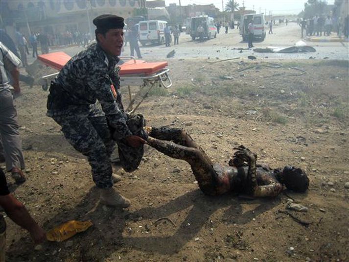 Íraskur lögreglumaður dregur á brott lík eftir sprengjutilræðið.