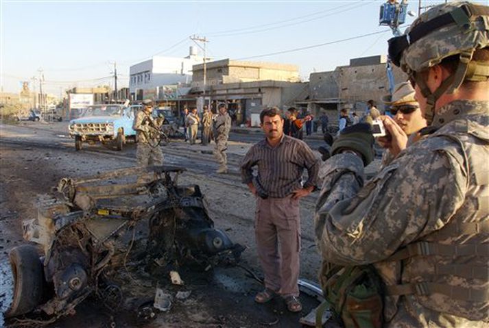 Bandarískur hermaður tekur mynd af bílflaki eftir bílsprenguárás í borginni Kirkuk í dag.