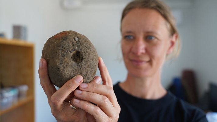 Liv Stidsing Reher-Langberg, fornleifafræðingur frá Moesgaard-safninu, heldur á kljástein sem notaður var við vefnað og fannst í uppgreftrinum nærri Árósum.