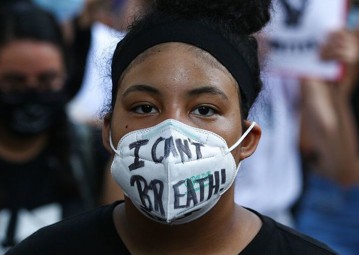 Þessi grímuklædda unga kona tók þátt í mótmælum í Houston. Á grímunni eru ein hinstu orð George Floyd og Erics Garner.